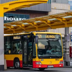 Żółto-czerwony autobus miejski na przystanku. Kierowca autobusu, zastanawiający się ile zarabia, czeka na pasażerów.