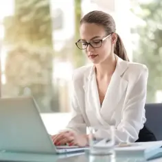 Kobieta w okularach pracuje na laptopie, przygotowując dokumenty. Może to być początek jej nierejestrowanej działalności gospodarczej.