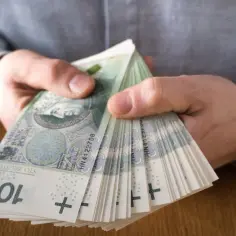 Dłonie trzymające stos banknotów 100 zł. Taka dyspozycja na wypadek śmierci zapewnia spokój bliskim.