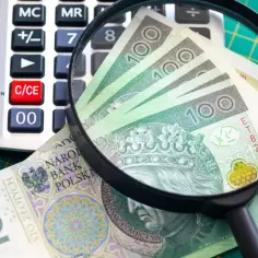 Pod lupą banknoty 100 zł i kalkulator. Analiza zarobków klasy średniej.