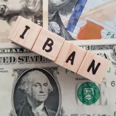 Drewniane klocki z literami IBAN leżą na banknotach dolarowych.