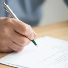 Dłoń podpisuje umowę dzierżawy. Dokument leży na drewnianym biurku, a osoba używa długopisu.