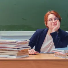 Nauczycielka zamyślona nad stertami prac, marząca o lepszych zarobkach nauczycieli w 2026 roku.