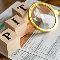 Drewniane klocki z literami P, I, T leżą na formularzu PIT-36. Lupa przybliża szczegóły dokumentu, sugerując analizę tego, co to jest PIT-36.