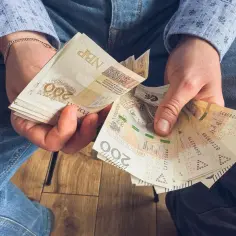 Dłonie trzymające stos banknotów 200 zł. To zapewne wynagrodzenie za urlop, które pozwoli na zasłużony odpoczynek.