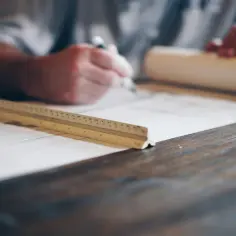 Architekt rysuje plany, zastanawiając się, ile zarabia. Na stole leży linijka i zwój papieru.