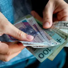 Dłonie trzymające polskie banknoty. Czy to wystarczy na pokrycie minimalnej stawki godzinowej?