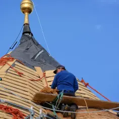 Doświadczony cieśla układa drewniane łuski na dachu wieży, pracując na wysokościach.