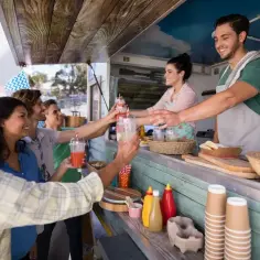 Uśmiechnięty barman podaje napoje grupie przyjaciół przy food trucku.