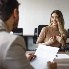 Uśmiechnięta kobieta podczas rozmowy kwalifikacyjnej, która może zakończyć się podpisaniem umowy na czas nieokreślony.