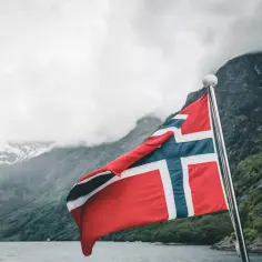 Norweska flaga na tle fiordu. Marzenie o pracy w Norwegii staje się rzeczywistością.