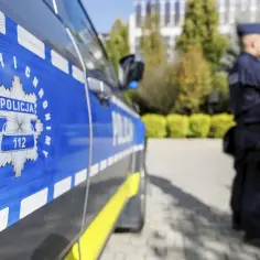 Policjant w mundurze stoi obok radiowozu. Czy jego zarobki w policji są adekwatne do służby?