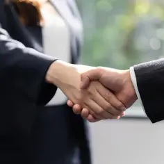 Dwie osoby w garniturach ściskają sobie dłonie. To symboliczny gest, który może zapowiadać jawność wynagrodzeń 2026.