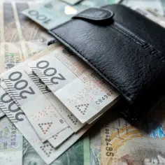 Czarny portfel na stosie polskich banknotów 200 zł. Zastanawiasz się, ile wynosi najniższa krajowa?
