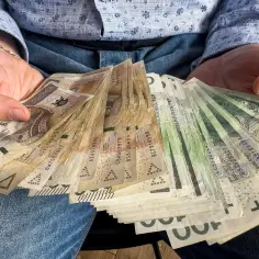 Ręce trzymające stos banknotów 100, 200 i 50 zł. To darowizna od rodziców na nowy cel.