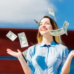 Szczęśliwa kobieta rzuca pieniędzmi w powietrze, symbolizując wysoki stawka godzinowa netto i sukces finansowy.