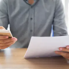 Mężczyzna trzyma telefon i dokumenty, sprawdzając potwierdzenie przelewu.
