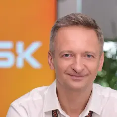 Uśmiechnięty mężczyzna w białej koszuli na tle logo GSK.