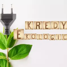 Wtyczka elektryczna wyrasta z zielonych liści, obok drewniane klocki z napisem "KREDYT EKOLOGICZNY".