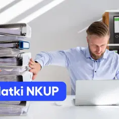 Mężczyzna przy biurku z laptopem i stosem segregatorów. Napis "Wydatki NKUP" sugeruje, że zajmuje się analizą kosztów.