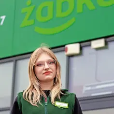 Natalia, pracownica Żabki, z uśmiechem pozuje przed sklepem.