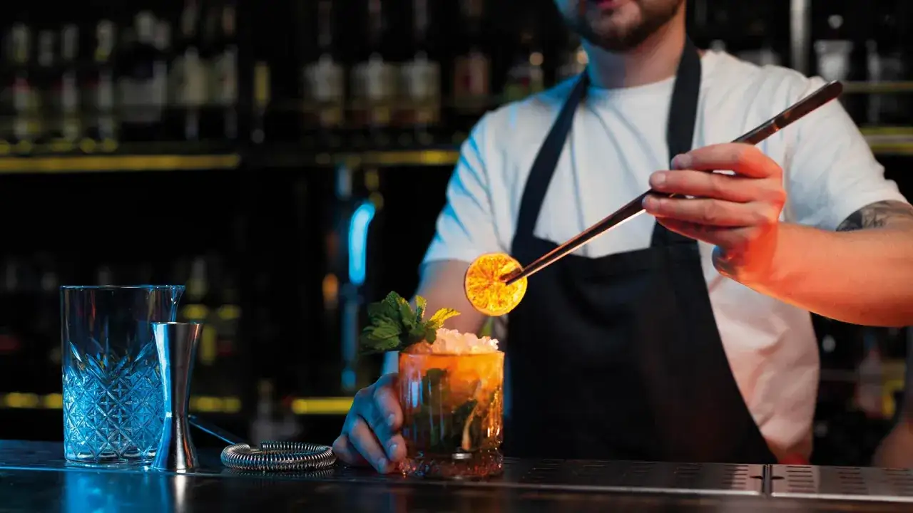 Doświadczony barman precyzyjnie ozdabia drinka płonącym plasterkiem pomarańczy.