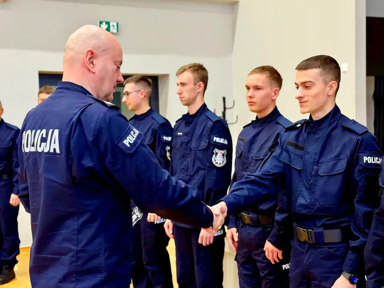 Policjant gratuluje młodym funkcjonariuszom. Dobre zarobki w policji to motywacja do służby.
