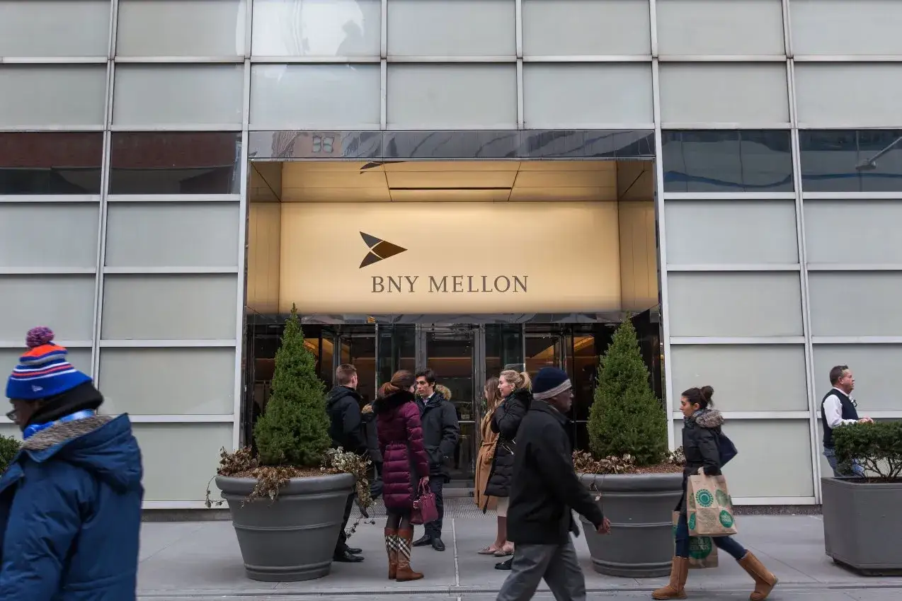 Ludzie przed wejściem do BNY Mellon. W tle widoczny neon z logo.