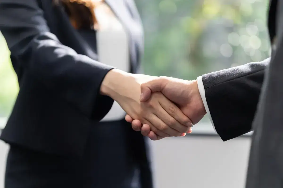 Dwie osoby w garniturach ściskają sobie dłonie. To symboliczny gest, który może zapowiadać nadchodzącą jawność wynagrodzeń w 2026 roku.