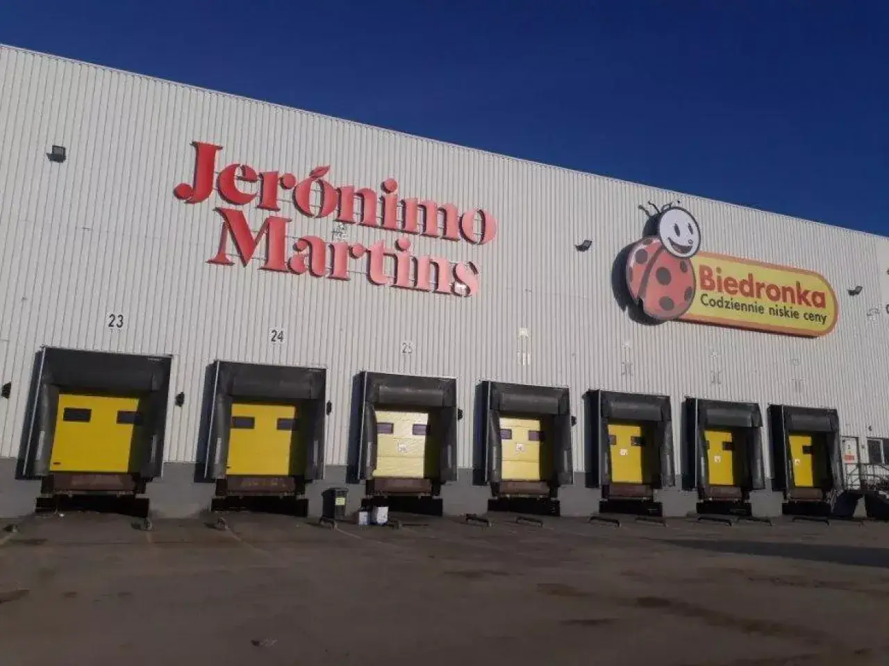 Magazyn Jeronimo Martins z logo Biedronki. Kilka ramp załadunkowych z żółtymi drzwiami.