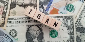 Drewniane klocki z literami IBAN leżą na banknotach dolarowych.