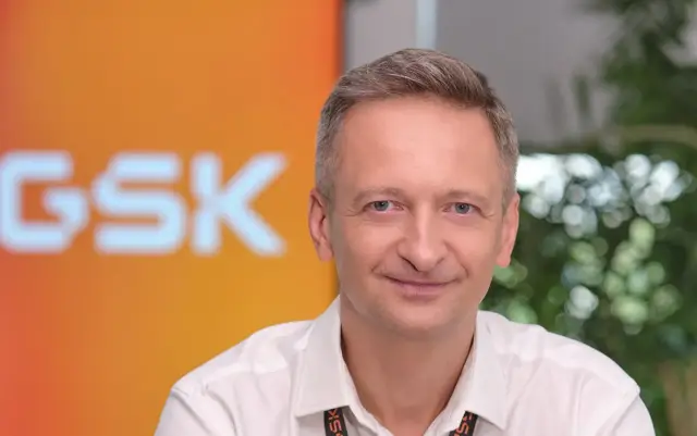 Uśmiechnięty mężczyzna w białej koszuli na tle logo GSK.